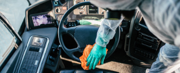 A person in a hazmat suit cleans a bus steering wheel with a microfiber cloth